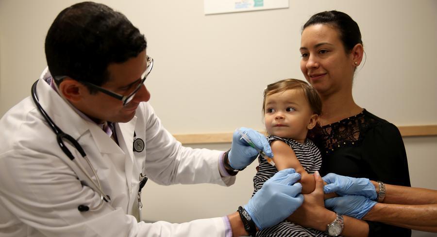 A woman holds her daughter as a pediatrician administers a measles vaccination. 